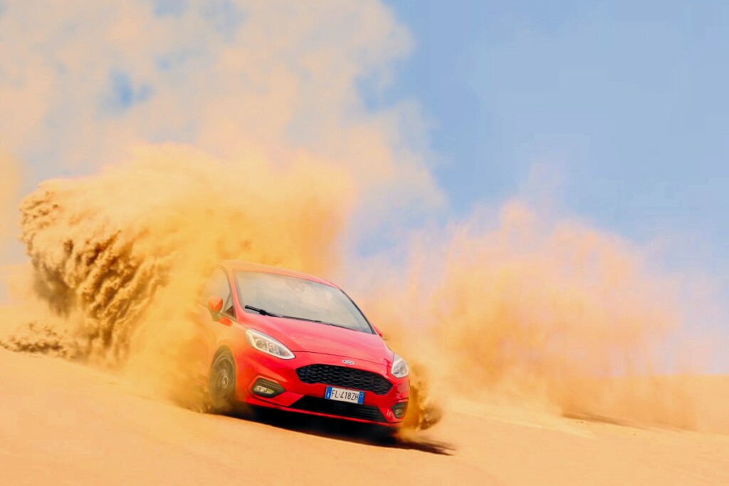 red ford focus vehicle driving on sand under blue daytime sky